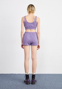 Un reggiseno sportivo in cotone viola abbinato a pantaloni corti con cintura elastica, abbinati a stivali neri e viola con lacci.