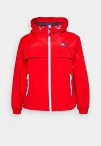 Czerwona wodoodporna kurtka z białymi zamkami błyskawicznymi, regulowanym kapturem i kieszenią na piersi. Posiada elastyczne mankiety i sportowy, casualowy design.