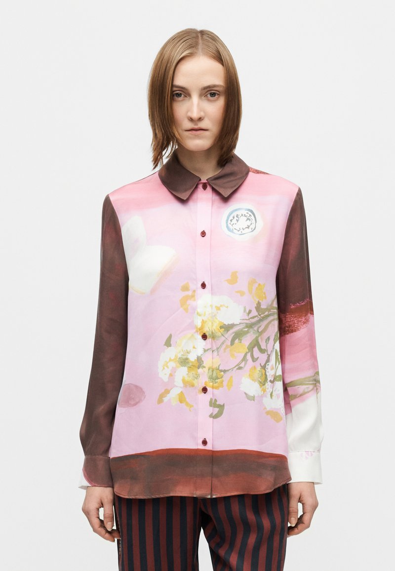 Rožinė gėlėta palaidinė su rudu apykakliu, ilgomis rankovėmis ir sagomis. Turi tekstūruotą gėlių raštą ir kontrastingą dryžuotą detalę apačioje.