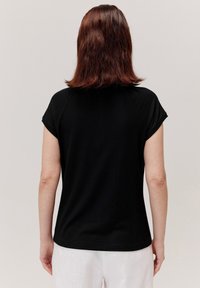 Czarna, prążkowana koszulka z krótkimi rękawami raglanowymi, okrągłym dekoltem i luźnym krojem. Materiał wydaje się miękki z delikatną teksturą.