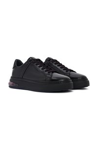 Par de zapatillas negras de cuero de caña baja con cordones negros y suelas gruesas negras que presentan amortiguación de aire visible en el talón.