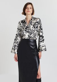 Donna che indossa una blusa a maniche lunghe a fiori bianco e nero infilata in una gonna in pelle nera a vita alta con uno spacco che arriva fino alla coscia.