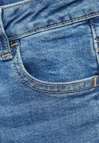 Plavi denim materijal s vidljivim šavovima, koji ima otvor za džep. Tekstura je glatka s blago izblijedjelim izgledom.