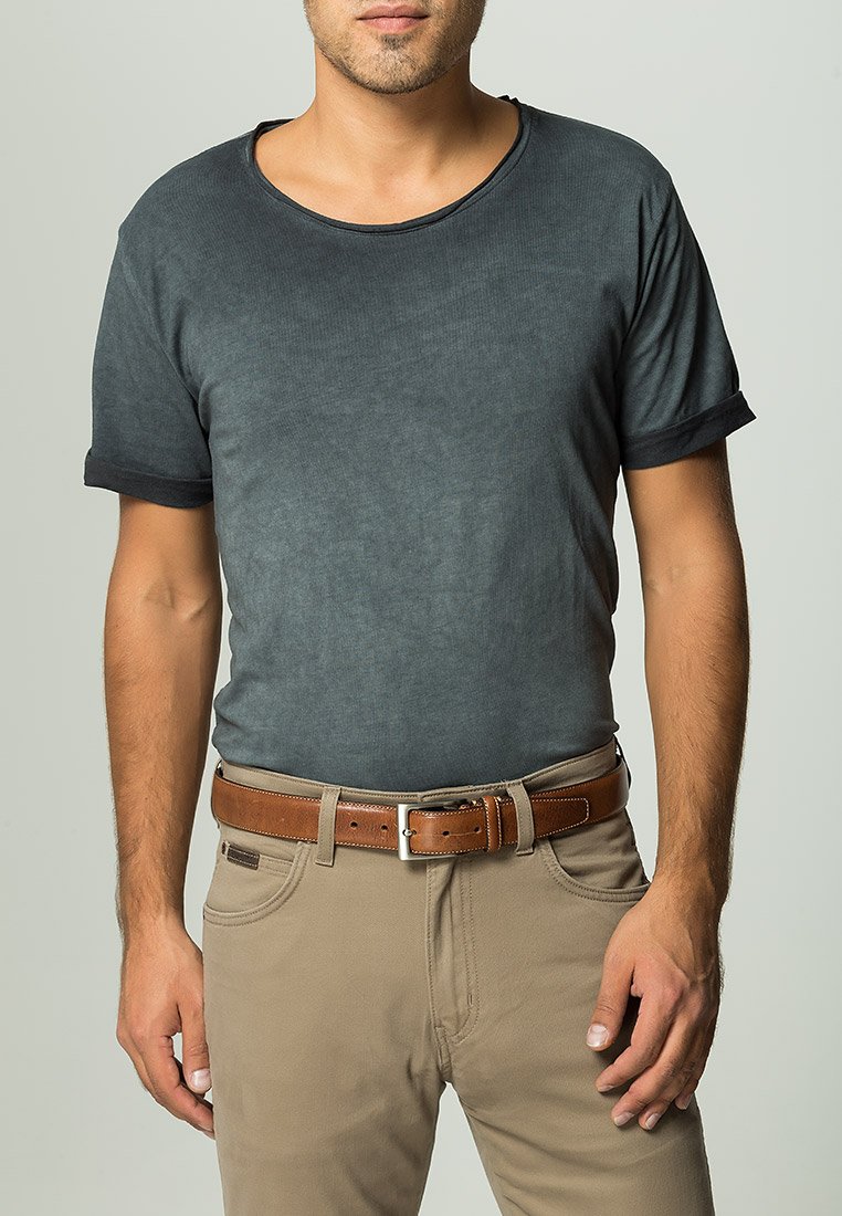 Urin grå T-shirt med rund hals och rullade ärmar, bärs tillsammans med beige byxor och ett brunt läderbälte med en silverfärgad spänne.