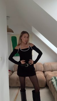 Black dress with halter neckline, long sleeves, and white piping. Worn with a wide black belt and knee-high black boots.