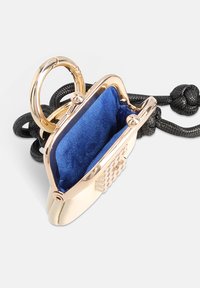 Porte-monnaie en métal doré avec intérieur en velours bleu, fermeture à charnière et bandoulière en cordon noir. Présente une surface texturée avec un détail de logo.