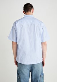 Chemise à manches courtes avec des rayures verticales bleues et blanches, design col, détail de dos yoke et coupe décontractée. Tissu en coton avec une légère texture.