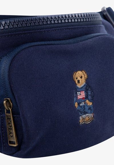 Mörkblå canvaspåse med dragkedja, försedd med en broderad björn i denim och ett flaggpatch. Guldtonade metalldetaljer med "POLO"-gravyren.