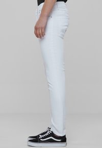 Jeans ajustados blancos hechos de denim, con un diseño de cinco bolsillos y una cintura de altura media. Combinados con zapatillas negras.