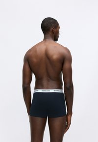 Σκούρο μπλε μπόξερ σορτς με λευκή ελαστική μέση που φέρει το λογότυπο "BJÖRN BORG", φορεμένα από ένα άτομο από πίσω, δείχνοντας μια λεία υφασμάτινη υφή.