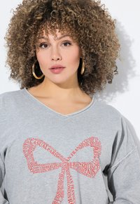 Grauer, übergroßer V-Ausschnitt-Sweatshirt mit einem roten Wortwolken-Design in Form einer Schleife, das Städtenamen zeigt. Weicher Stoff, lässiger Stil.
