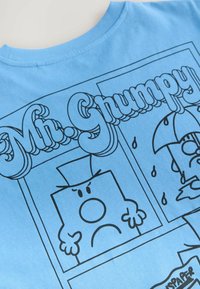 Ljusblå bomullströja med svarta linjeteckningar av en karaktär märkt "Mr. Grumpy" och ett paraply, tillsammans med regndroppar.
