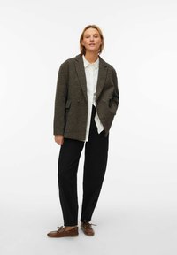 Rjav tweed suknjič z nazobčanim ovratnikom, dvema gumboma in sprednjimi žepi, kombiniran z belo srajco, črnimi hlačami in rjavimi čevlji.