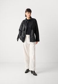 Sort læderjakke med frynse detaljer, knaplukning, lange ærmer, parret med off-white kordfløjl bukser og sorte hælede ankelstøvler.