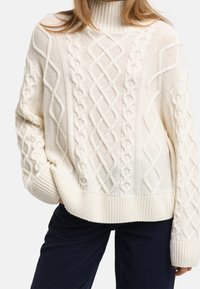 Chunky knit cream sweater with a high neckline, featuring cable patterns, ribbed cuffs, and hem. Soft, textured fabric.