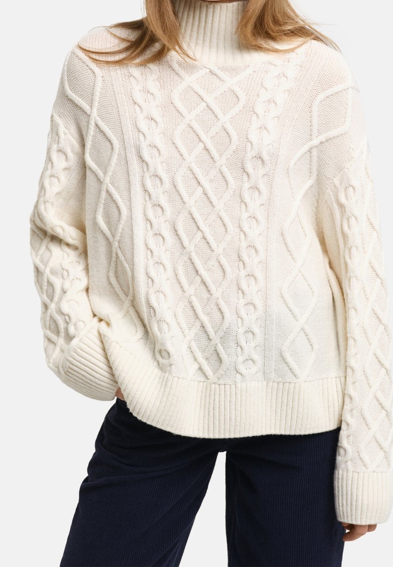 Chunky knit cream sweater with a high neckline, featuring cable patterns, ribbed cuffs, and hem. Soft, textured fabric.
