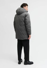 Pelēka, polsterēta jaka ar kapuci, ar elegantu dizainu un vidusceļgala garumu. Kombinēta ar melnām pieguļošām biksēm un apaviem.