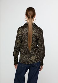 Leopard print shirt in olive and black, long sleeves, button cuffs, relaxed fit, paired with dark denim pants. Smooth, lightweight fabric.