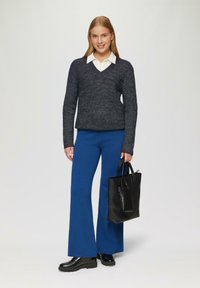 Granatowy sweter w serek, niebieskie szerokie spodnie i czarna torebka. Modelka nosi błyszczące czarne botki za kostkę; widoczne szczegóły tekstury materiału.