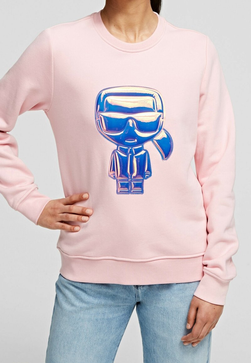 Felpa rosa con una grafica lucida di un personaggio stilizzato con occhiali da sole. Il design ha una vestibilità comoda con polsini e orlo a costine.