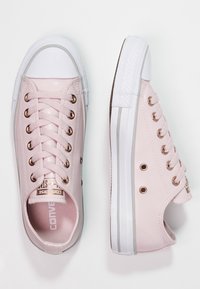 Paire de baskets basses Converse de couleur rose pâle avec embouts en caoutchouc blancs et semelles blanches, présentées en vues de dessus et de côté.