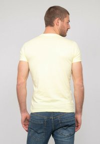 T-shirt jaune à manches courtes au design ajusté, fabriqué en tissu doux ; associé à un jean en denim bleu avec des poches arrière.