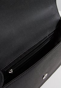 Borsa a mano in pelle nera con texture, dotata di un interno liscia, che presenta una tasca con zip e una chiusura a scatto metallica.
