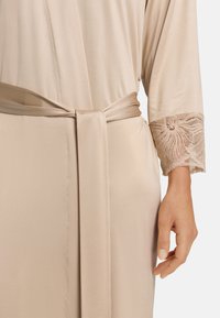 Accappatoio beige in satin con cintura e dettagli in pizzo sulle maniche. Texture liscia con un delicato motivo in pizzo ai polsi.