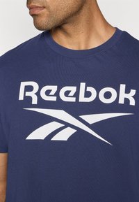 Blue cotton t-shirt featuring a large white Reebok logo and an aerodynamic graphic design on the front. Crew neck and short sleeves.