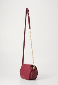Red leather crossbody bag with a textured finish, featuring a gold chain accent, adjustable strap, and a front flap pocket.