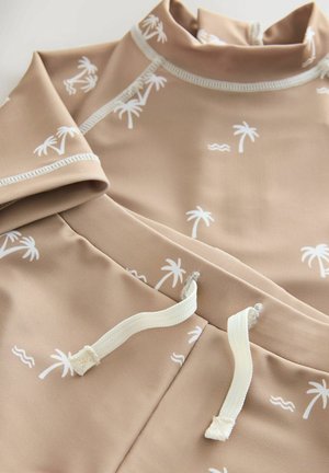 Beige rash guard with white palm tree print; features a high collar, short sleeves, and drawstrings on the hem for adjustment.