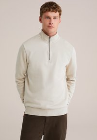 Felpa con zip beige, dotata di colletto alto, polsini e orlo a costine; realizzata in un tessuto liscio e morbido; design minimalista senza motivi o dettagli.