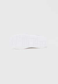 Λευκή σόλα παπουτσιού που φαίνεται από κάτω, με μοτίβο πλέγματος και το λογότυπο Calvin Klein στο κέντρο.