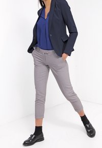 Granatowa marynarka na niebieskiej bluzce, jasnoszare, dopasowane spodnie cygaretki oraz czarne mokasyny z skarpetkami. Gładkie tekstury i dopasowany krój.