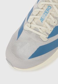 Close-up of a gray and blue running shoe toe with mesh fabric, cream laces, and "ADIZERO" printed on the tongue.