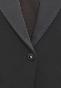 Blazer nero con colletto grigio testurizzato, chiusura con un solo bottone dorato e fodera interna liscia. Presenta rever affilati e una vestibilità sartoriale.