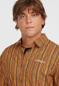 Langærmet skjorte med knapper i orange, brun og gulstribede mønstre med blomster. Har krave og broderet logo.