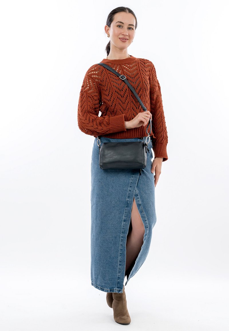 Maglione in maglia ruggine con motivi aperti, abbinato a una gonna maxi in denim con uno spacco laterale. Borsa a tracolla nera con hardware argentato. Stivaletti marroni.