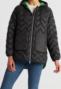 Giacca a vento nera trapuntata con cappuccio, con rivestimento verde, due tasche frontali e zip frontale. Motivo a diamante texturizzato su tutta la superficie.