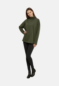 Top dolcevita verde oliva con spalle scese e maniche lunghe, abbinato a jeans skinny neri e stivaletti alla caviglia. Design semplice e casual.