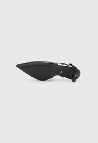 Zapato negro de tacón puntiagudo hecho de material sintético texturizado, con una delgada correa en el tobillo y una suela suave con un tacón bajo tipo bloque.