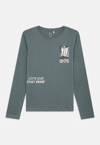 Camisa de manga longa verde feita de algodão, com uma estampa gráfica com o número "10" e a frase "VAMOS CHUTAR ALGUMA GRAMA" em branco.