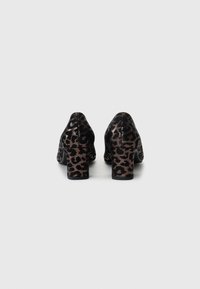 Black high-heeled shoes with a glossy finish and leopard print pattern in metallic gold. Chunky block heels and rounded toes.