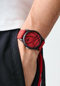 Sarkans basketbola laikrodis ar teksturētu sarkanu siksniņu un melnu korpusu. Iespējo apaļa sejas šķautne ar sarkanu ciparnīcu un melnu groza dizainu, sudraba akcents.