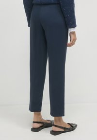 Pantaloni navy su misura con taglio dritto, texture liscia e vita media, abbinati a sandali neri con finitura lucida.