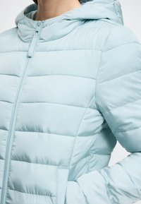 Ανοιχτό μπλε μπουφάν με οριζόντια καπιτονέ, κεντρικό φερμουάρ και κουκούλα. Λείωμα υφής και κομψός σχεδιασμός με πλαϊνές τσέπες.