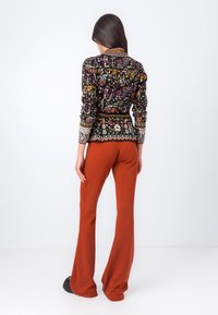 Cardigan nero a fantasia floreale con colori vivaci, vita aderente e polsini texturizzati, abbinato a pantaloni arancioni a campana.