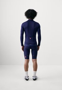 Navy Fahrradtrikot mit langen Ärmeln, enganliegendem Design und Rückentasche. Kombiniert mit passenden Shorts, die eine gepolsterte Sitzfläche und reflektierende Akzente aufweisen.