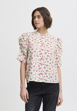 Bloem blouse met een crèmekleurige achtergrond, een roze bloemenpatroon, korte pofmouwen en een knoopsluiting aan de voorkant.