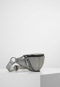 Harmaa nahkainen vyölaukku, jossa on pyöreä muoto, vetoketjukiinnitys ja säädettävä hihna. Ominaisuuksiin kuuluu sileä pinta ja minimalistinen muotoilu.